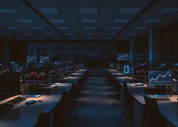 Empty crypto exchange office desks with market chart monitors representing Coinbase restructuring